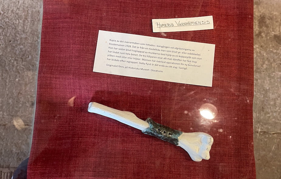 Copy of the humerus found in the cloister during the excavation of the monastery ruins in 1928. It is from a medieval man who had been injured by a sword or axe. He was then patched up by the monks using a copper plate wrapped around the entire leg. The three halves show that the plate was then fastened together with rivets or wood. The man has survived the operation because new bone tissue has formed after the procedure. This find is the only one of its kind in Sweden. The original is in the Historiska Museet in Stockholm.